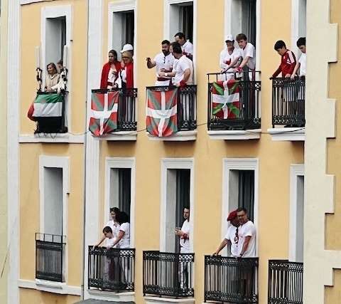 People on balconies of yellow building with white trim at the San Termini Opening Ceremony in Northern Spain
